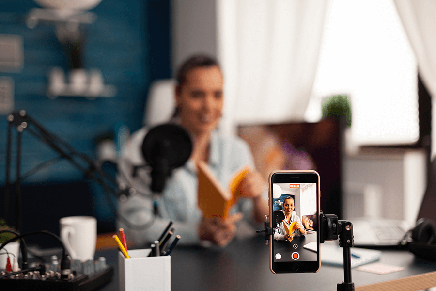 Young woman sitting in front of Iphone recording a book review