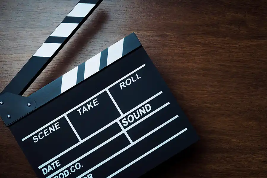 A film clacker resting on a dark wood table. The arm of the clacker is raised up at an angle