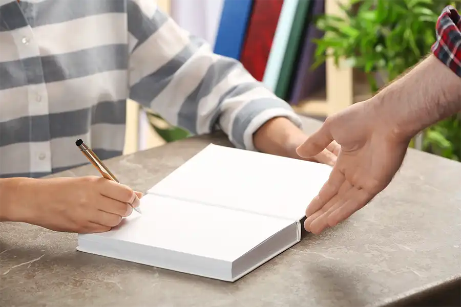 Writer signing an autograph in book at table for one of their readers.