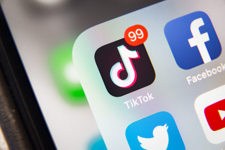 TikTok and Facebook application  on screen Apple iPhone XR Handwritten sketch notes in a notebook on dark wooden table with a yellow coffee cup and black pen laying next to it