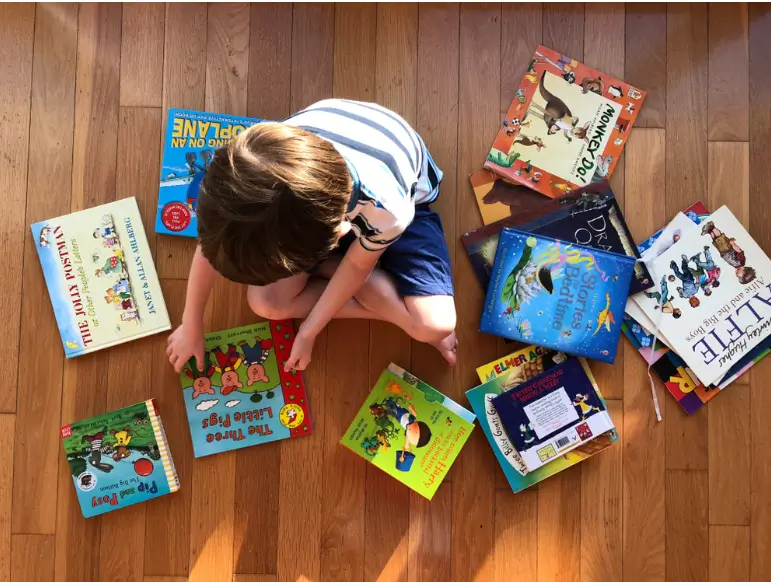 top-down view of a child sitting on a wooden floor surrounded by children’s books