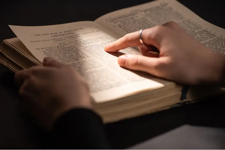 a hand pointing at a passage from Genesis in an open Bible with a light shining on it